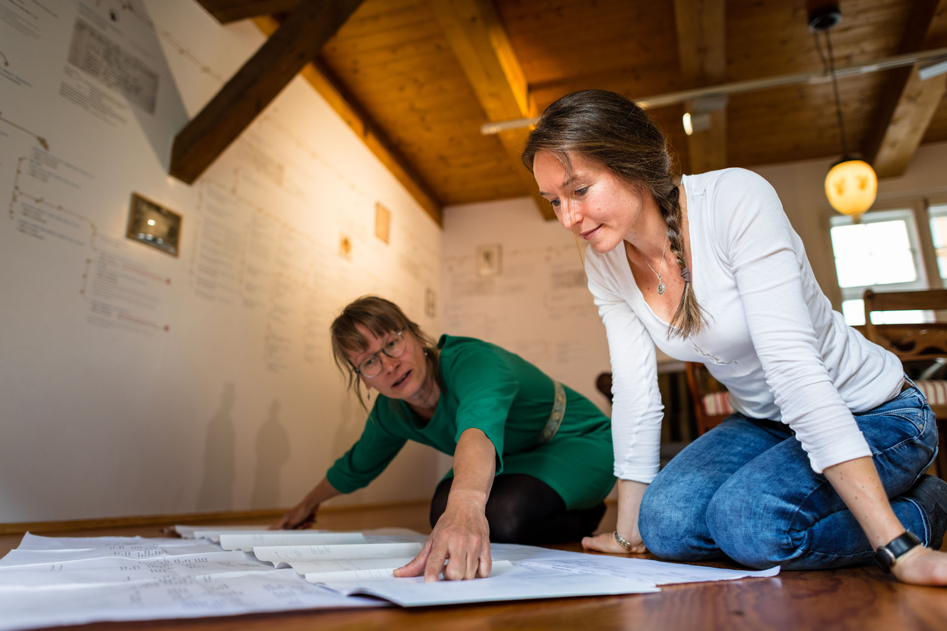 Two women kneel over a large paper and research the family tree of Caspar David Friedrich.